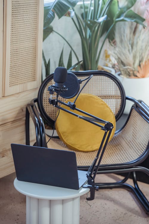 Modern laptop and microphone on tripod placed near wicker chair in modern studio before recording podcast
