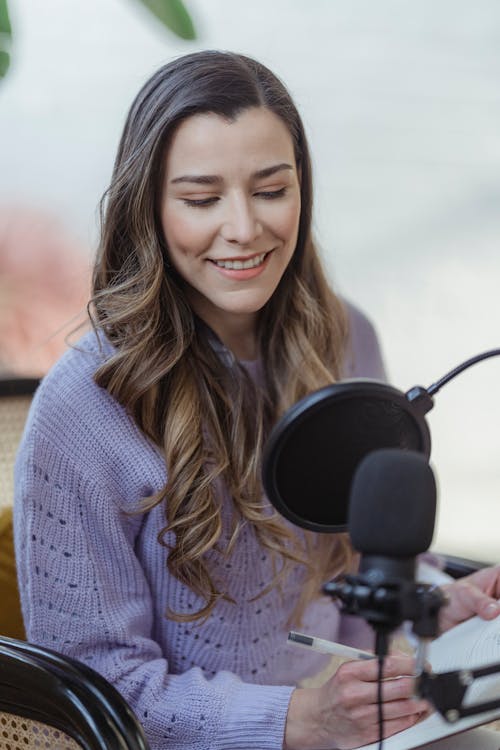 Free Smiling woman writing in planner while recording podcast Stock Photo