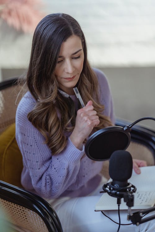 Woman with notebook recording podcast on microphone