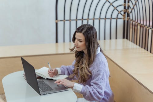 Focused woman browsing laptop and writing notes in notebook