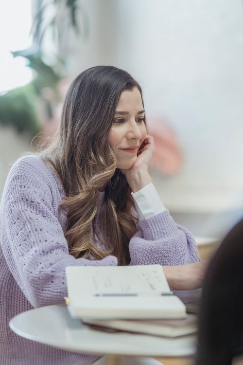 Free Serious female teleworker touching chin while doing online work on netbook at table with notebooks Stock Photo