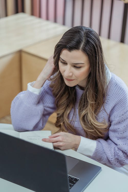 Free High angle of concentrated female employee watching netbook while taking notes in planner during online work Stock Photo