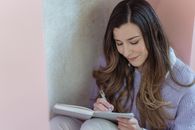 High angle of positive female with long wavy hair writing thoughts in notepad