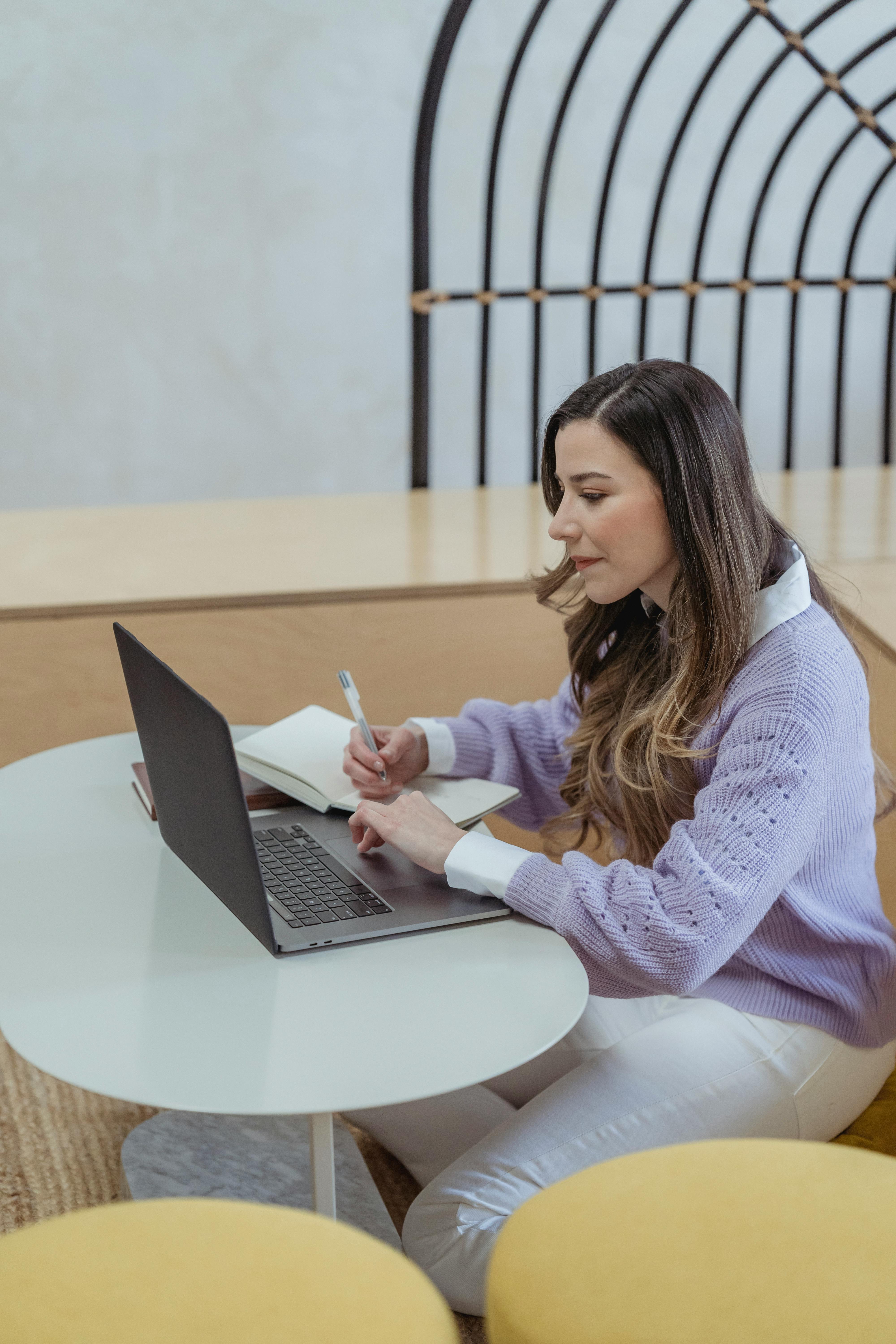 focused woman writing in diary and browsing laptop