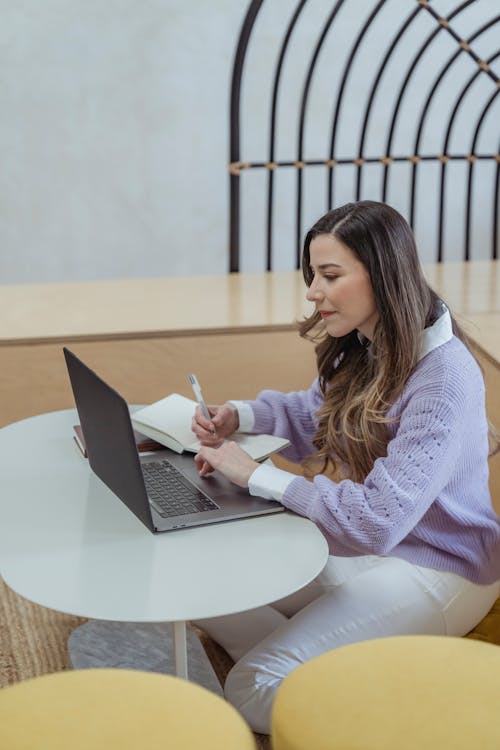 Focused woman writing in diary and browsing laptop