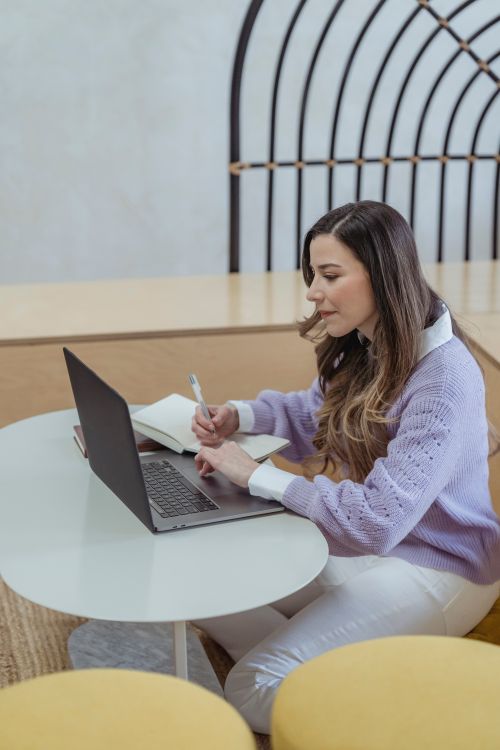 Free High angle of concentrated female remote worker taking notes in planner while using netbook at table Stock Photo
