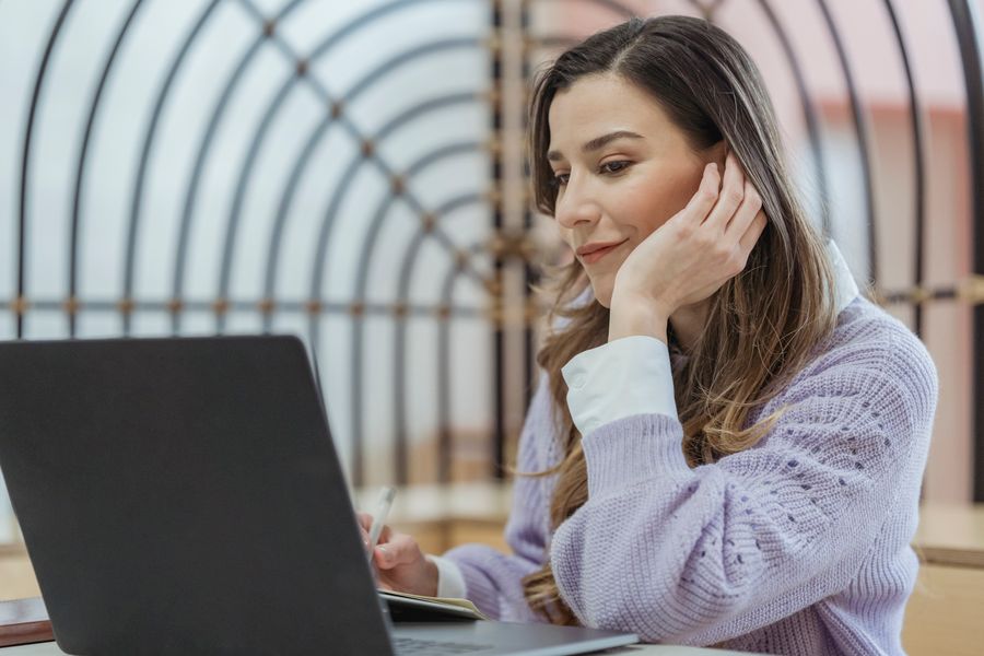 Smiling female teleworker leaning on hand while taking notes in planner during remote work at looking at screen