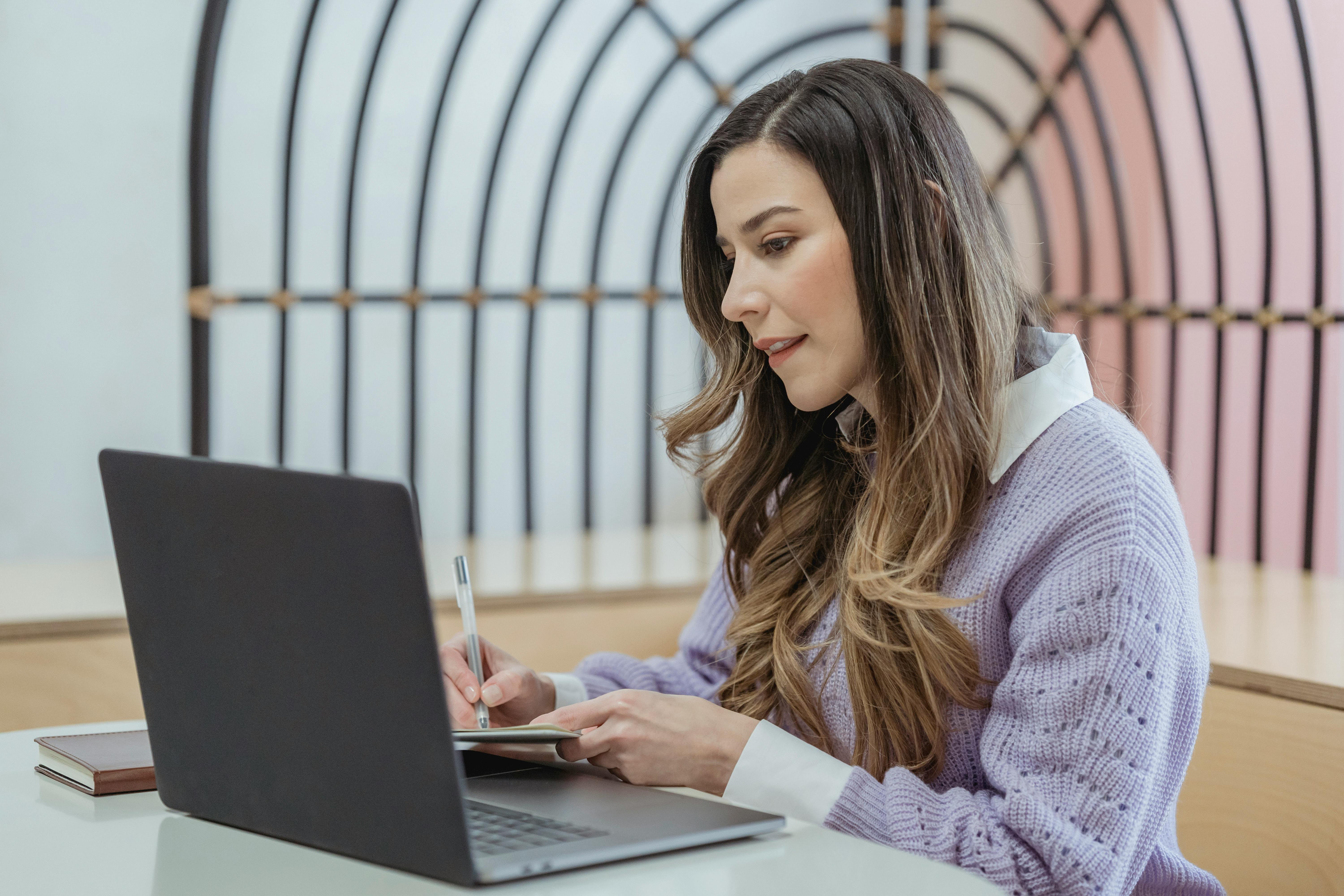 positive woman writing in notebook and watching laptop