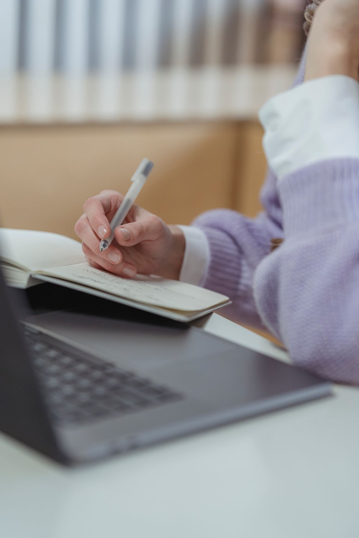 A person writing a presentation script and notes at a desk with a laptop