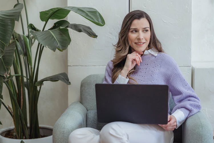 Positive Young Woman Working On Netbook Sitting In Armchair In Office