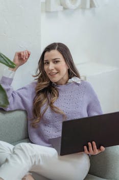 Young woman in a lavender sweater working on a laptop with a cheerful smile indoors.