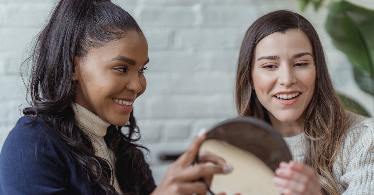 Happy young ethnic woman giving mirror to female client after applying makeup