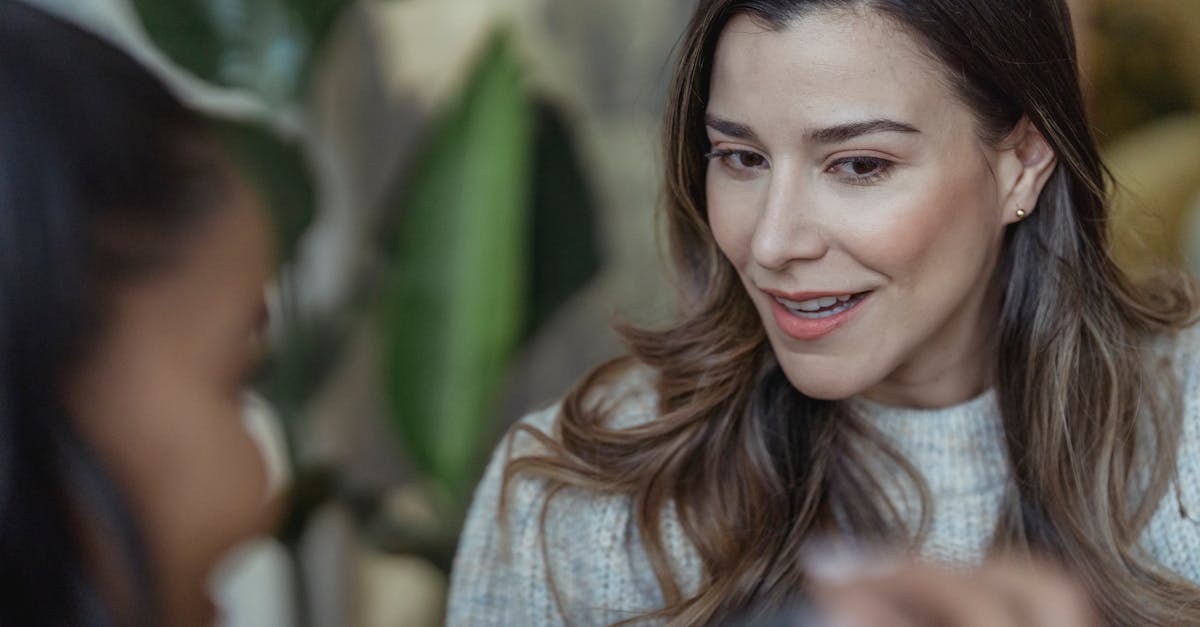 Crop unrecognizable African American female visagiste smiling and holding mirror in front of happy client with long wavy hair in beauty salon