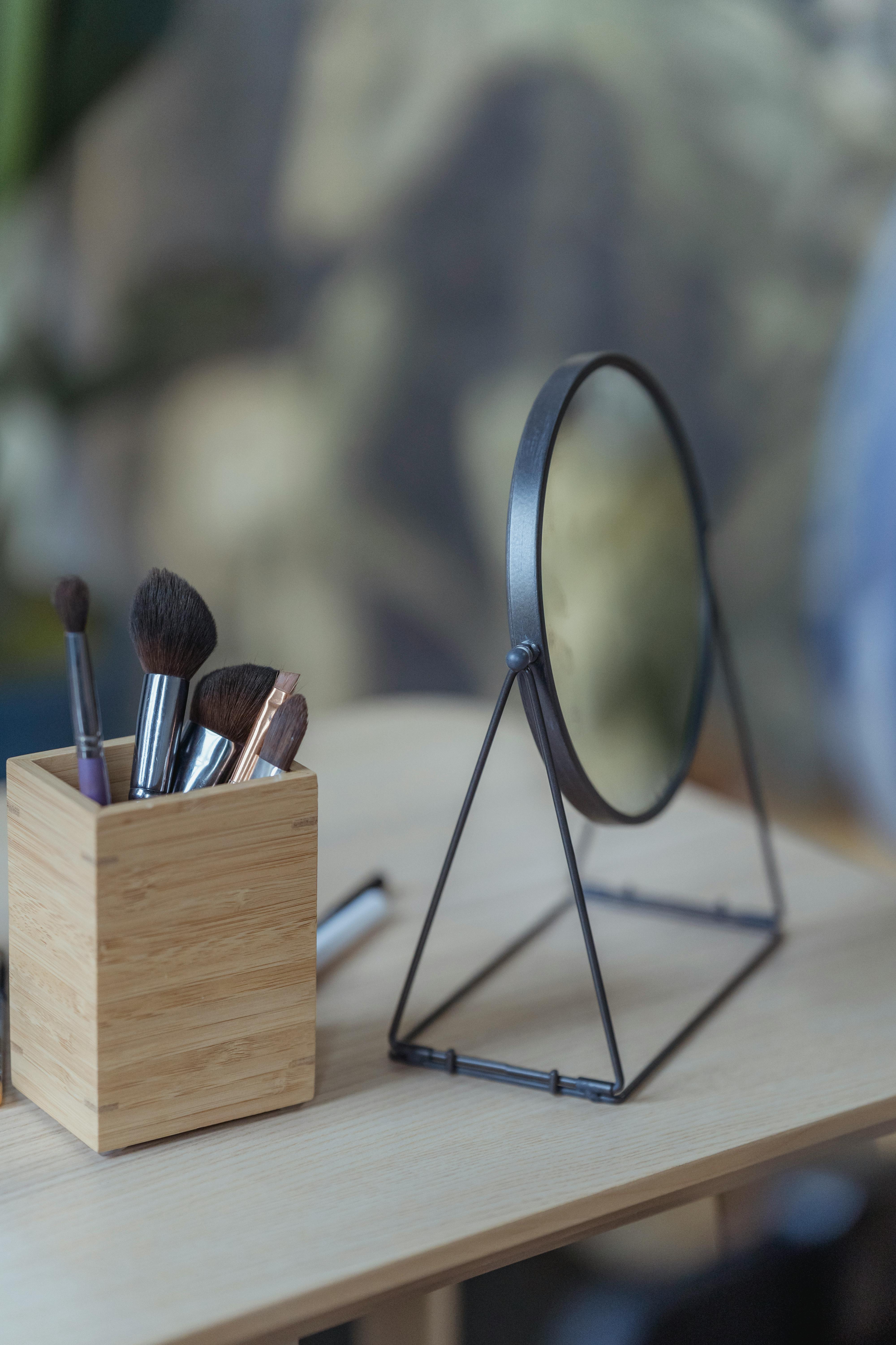 cosmetic brushes and round mirror placed on wooden table
