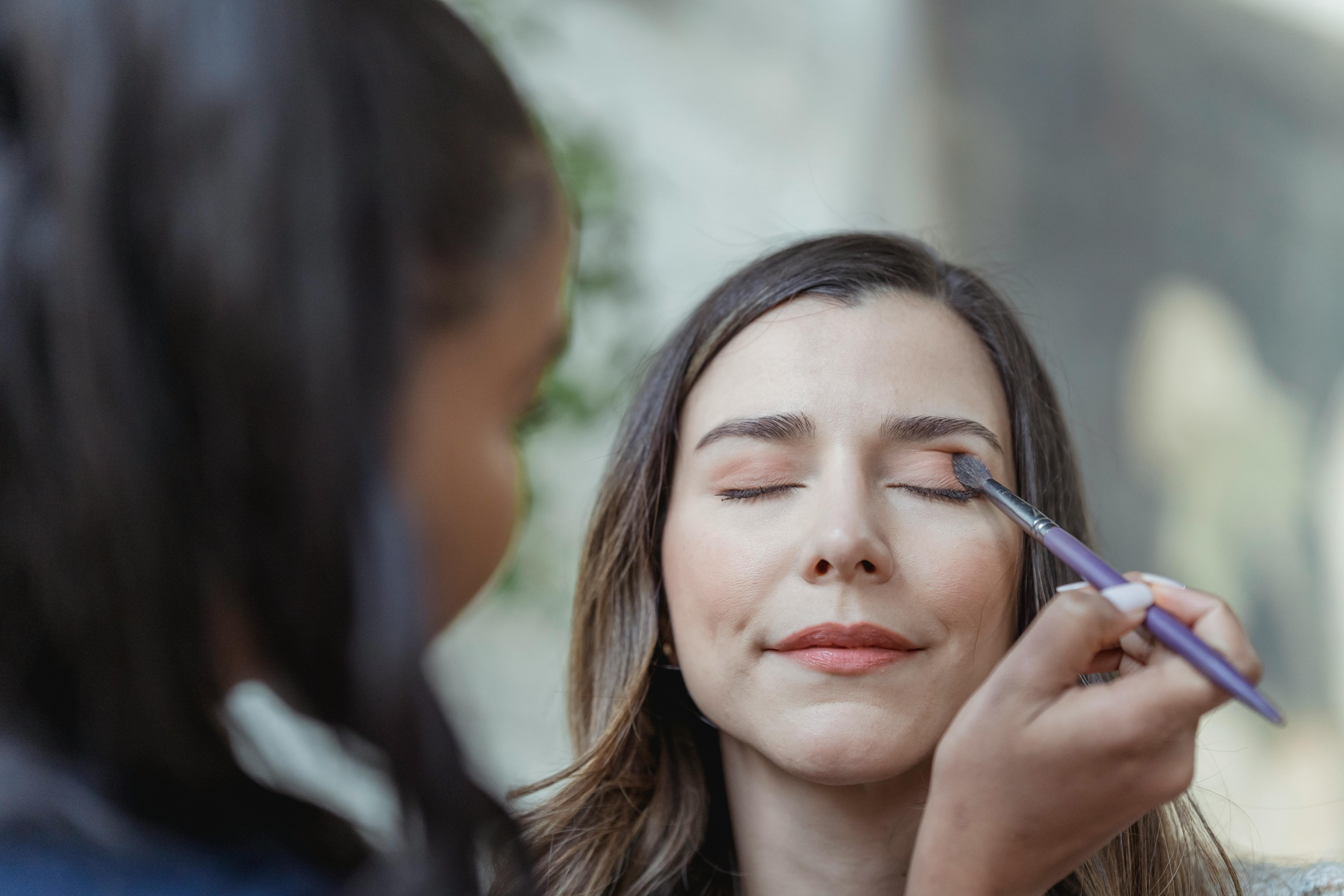 young black visagiste applying eyeshadow on eyelids of female customer