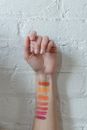 Crop unrecognizable woman holding hand near brick wall after testing of makeup products