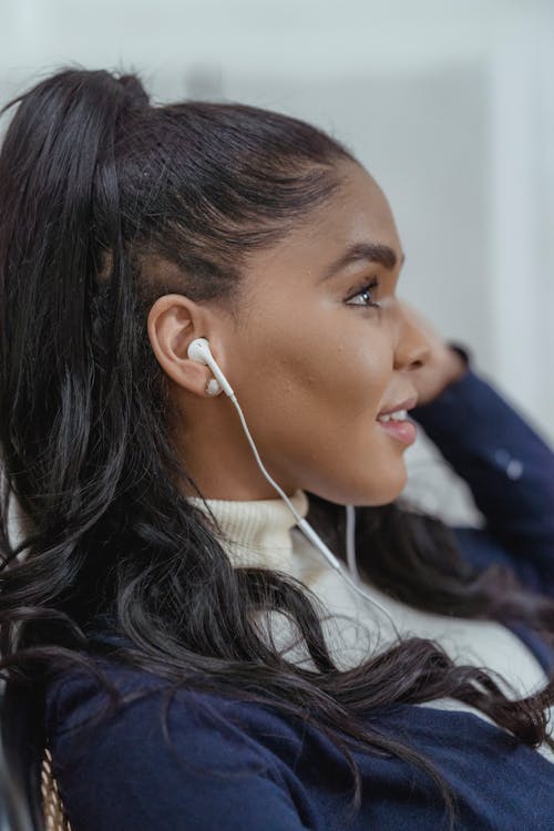 Smiling young ethnic woman enjoying music in earphones