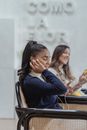 Cheerful young diverse female friends in earphone using smartphones in cafe