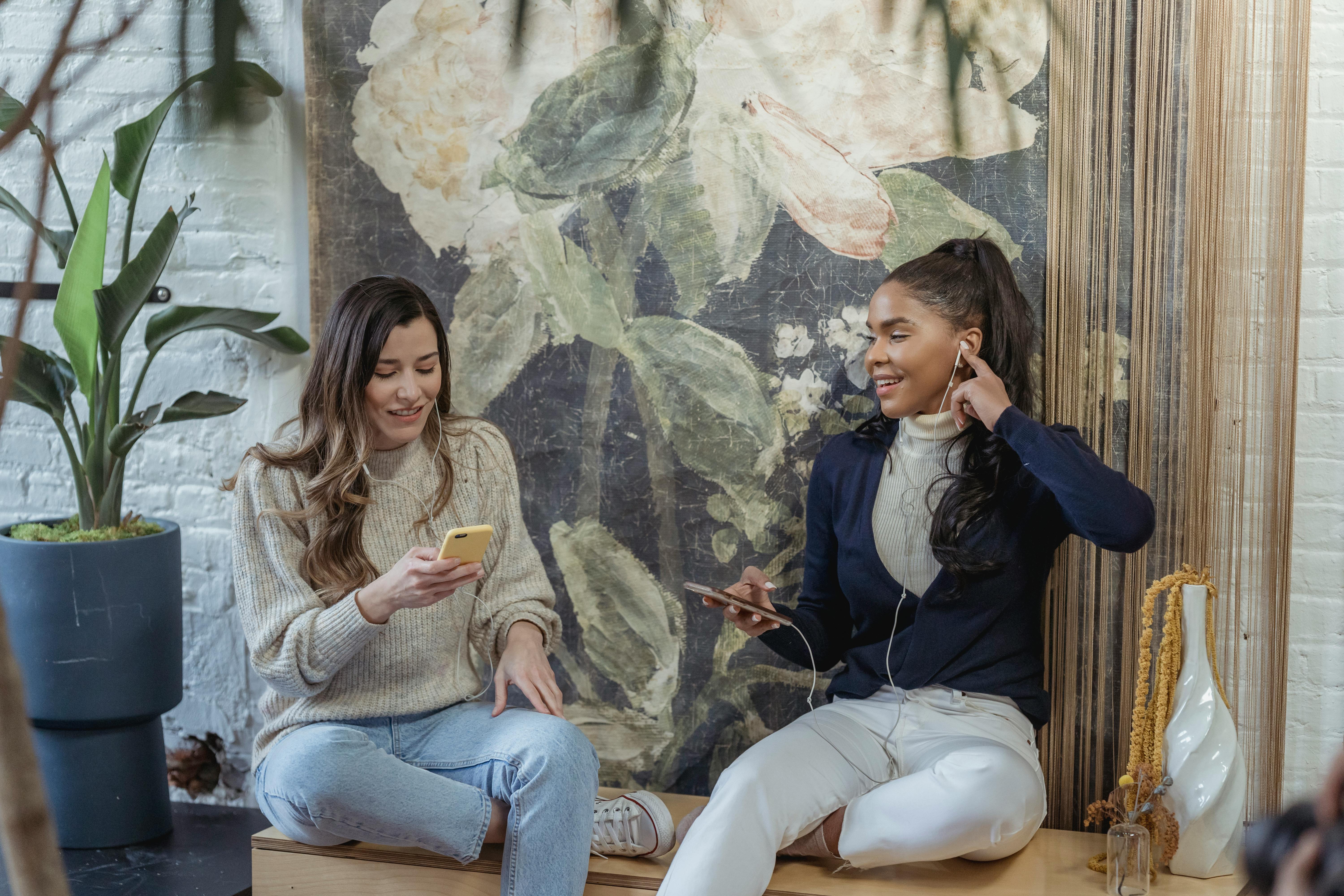 positive young multiracial female colleagues talking on smartphones during break in modern workspace