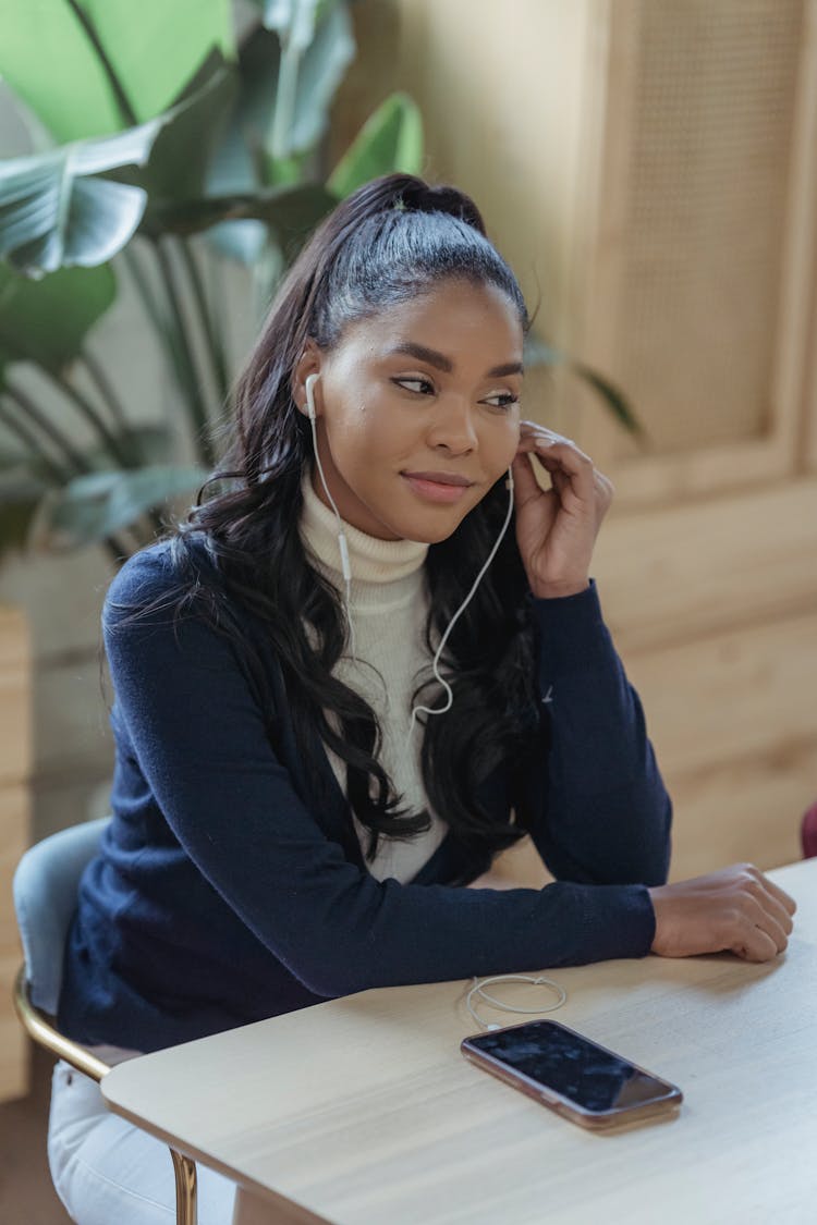 Positive Young Ethnic Lady Listening To Podcast At Table