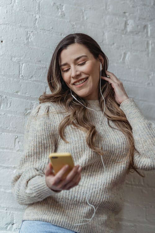 Cheerful woman with earphones listening to music with smartphone