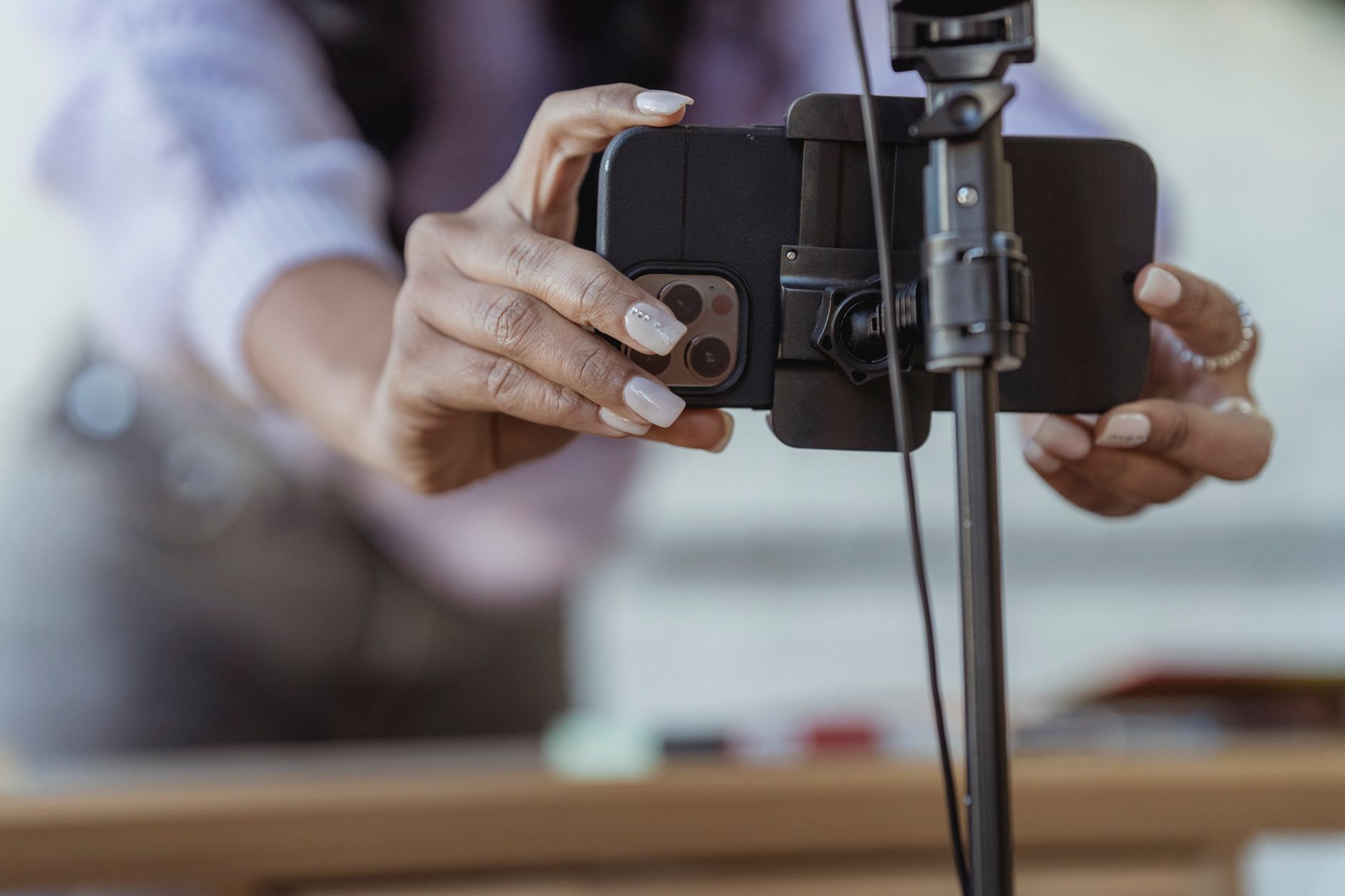 Crop unrecognizable female setting mobile phone on tripod while recording vlog on blurred background