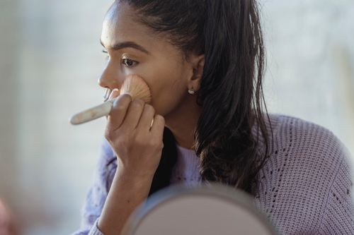 Free Concentrated crop African American young female spreading foundation cream on face with brush on blurred background Stock Photo