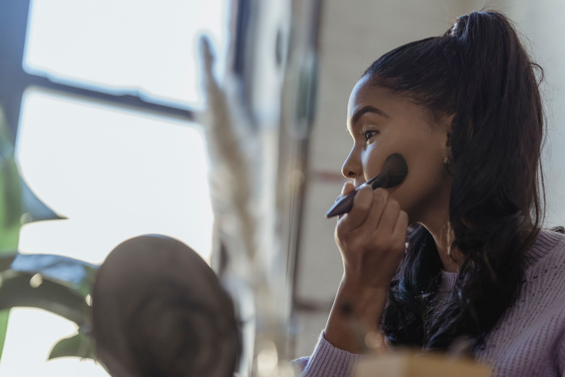 Side view of professional African American beautician spreading foundation on cheeks on blurred background