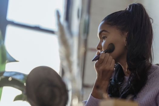 Side view of professional African American beautician spreading foundation on cheeks on blurred background