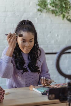 Focused African American beautician spreading powder on face with brush at table while having online video session