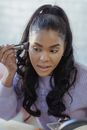 Focused black female visagiste applying makeup and looking away