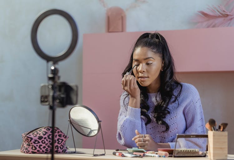 Charming Black Female Making Makeup And Filming Vlog In Light Studio