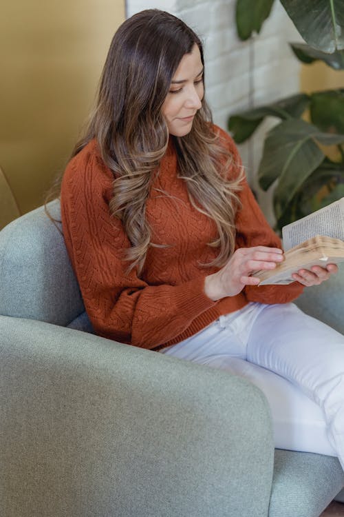 Free Concentrate woman with long hair in casual clothes sitting on armchair and reading interesting book in light room Stock Photo