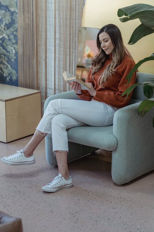 Free Calm female sitting on armchair and reading book Stock Photo