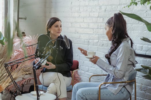 Two women engaged in a podcast interview with coffee indoors.