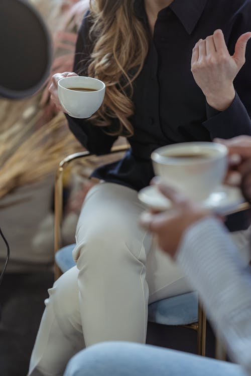 Free Crop anonymous female host talking to guest and having coffee while recording conversation on microphone Stock Photo