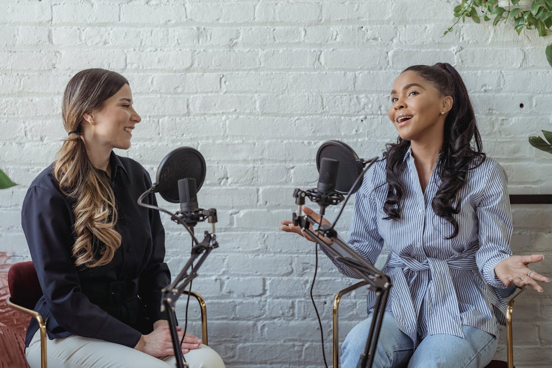 Free Smiling African American female guest gesticulating while having interview with journalist sitting near mic Stock Photo