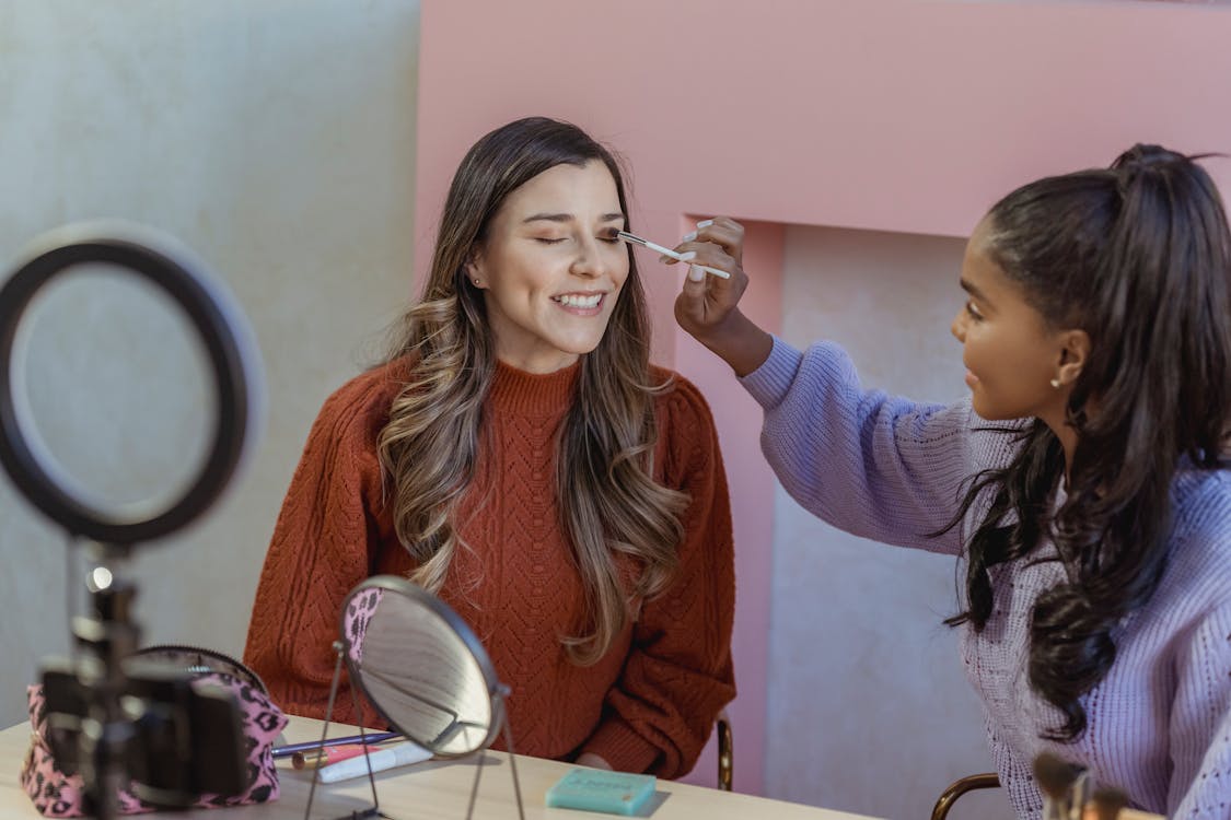 Free Black beauty blogger applying makeup on model during live broadcast Stock Photo