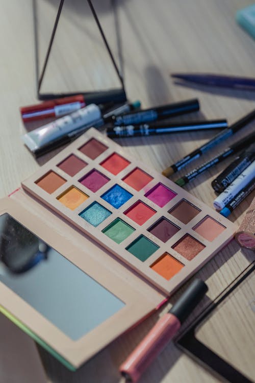 From above of various makeup supplies placed around eyeshadow pallet with mirror on table