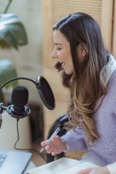 High angle of woman with opened notepad and pen talking in microphone under laptop