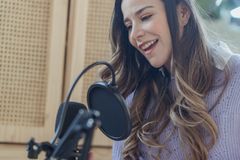 Content female in casual wear talking to professional microphone while recording audio record on chair with opened notebook in light room