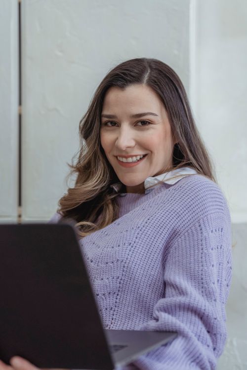 Free Positive female worker surfing internet on modern netbook while smiling and looking at camera in light room near white wall Stock Photo
