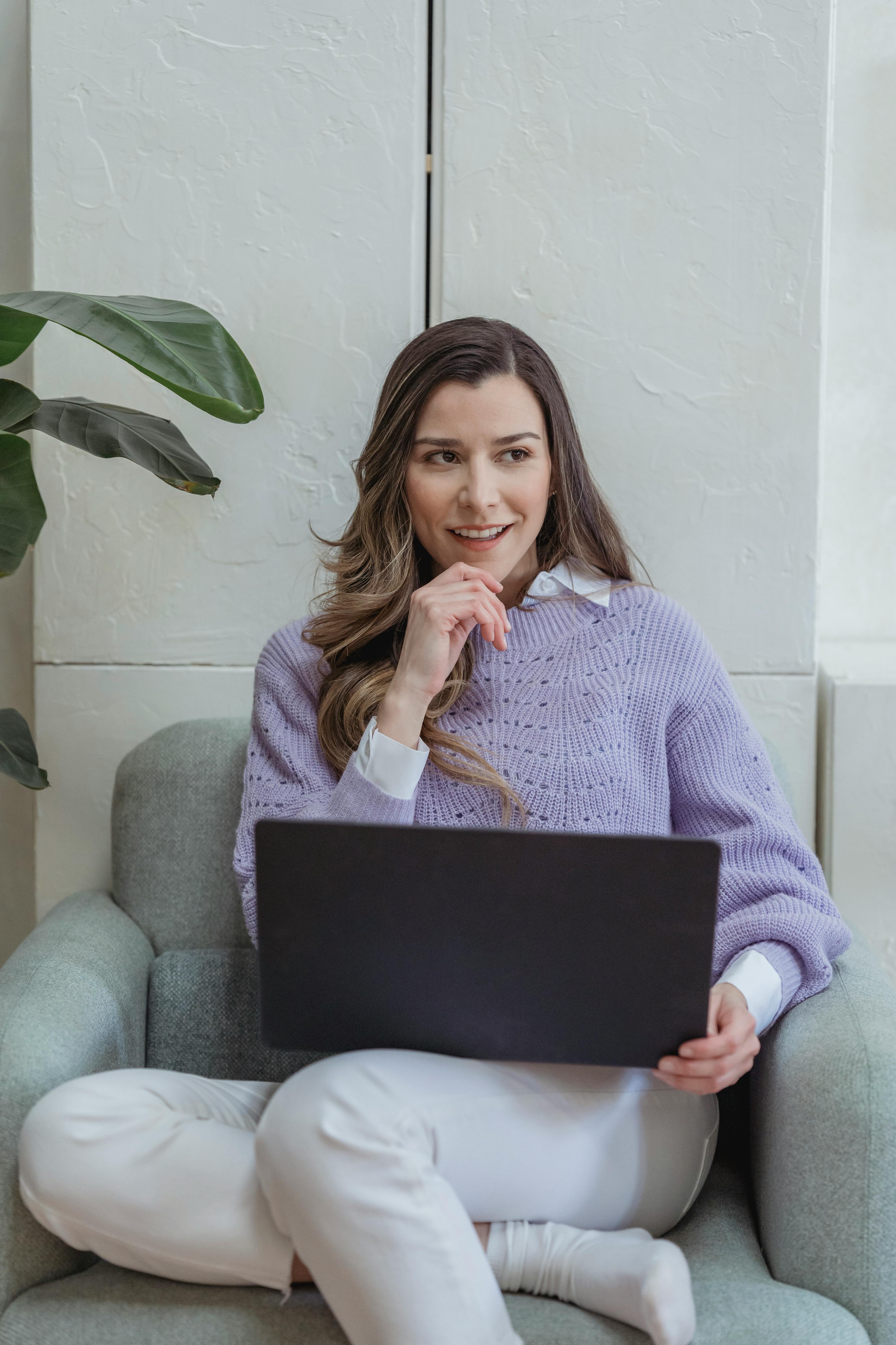 positive woman browsing laptop in armchair