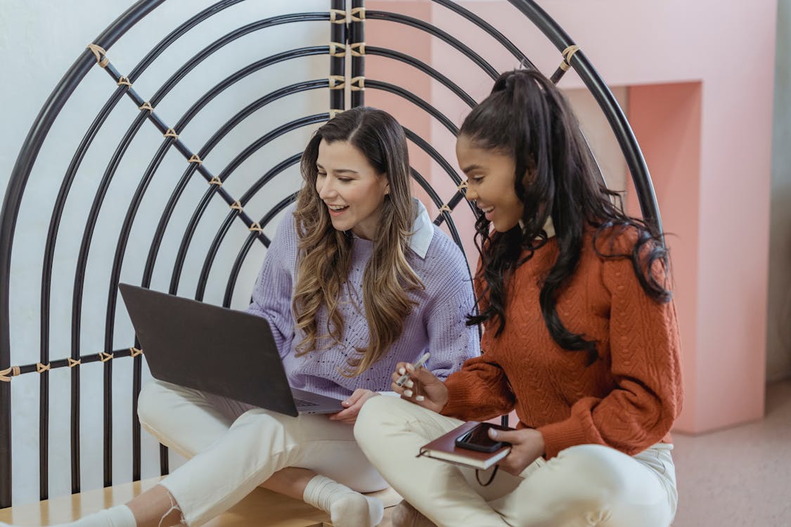 Cheerful diverse women using laptop on floor