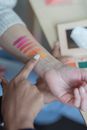 Crop faceless visagiste drawing cosmetic swatches on clients arm