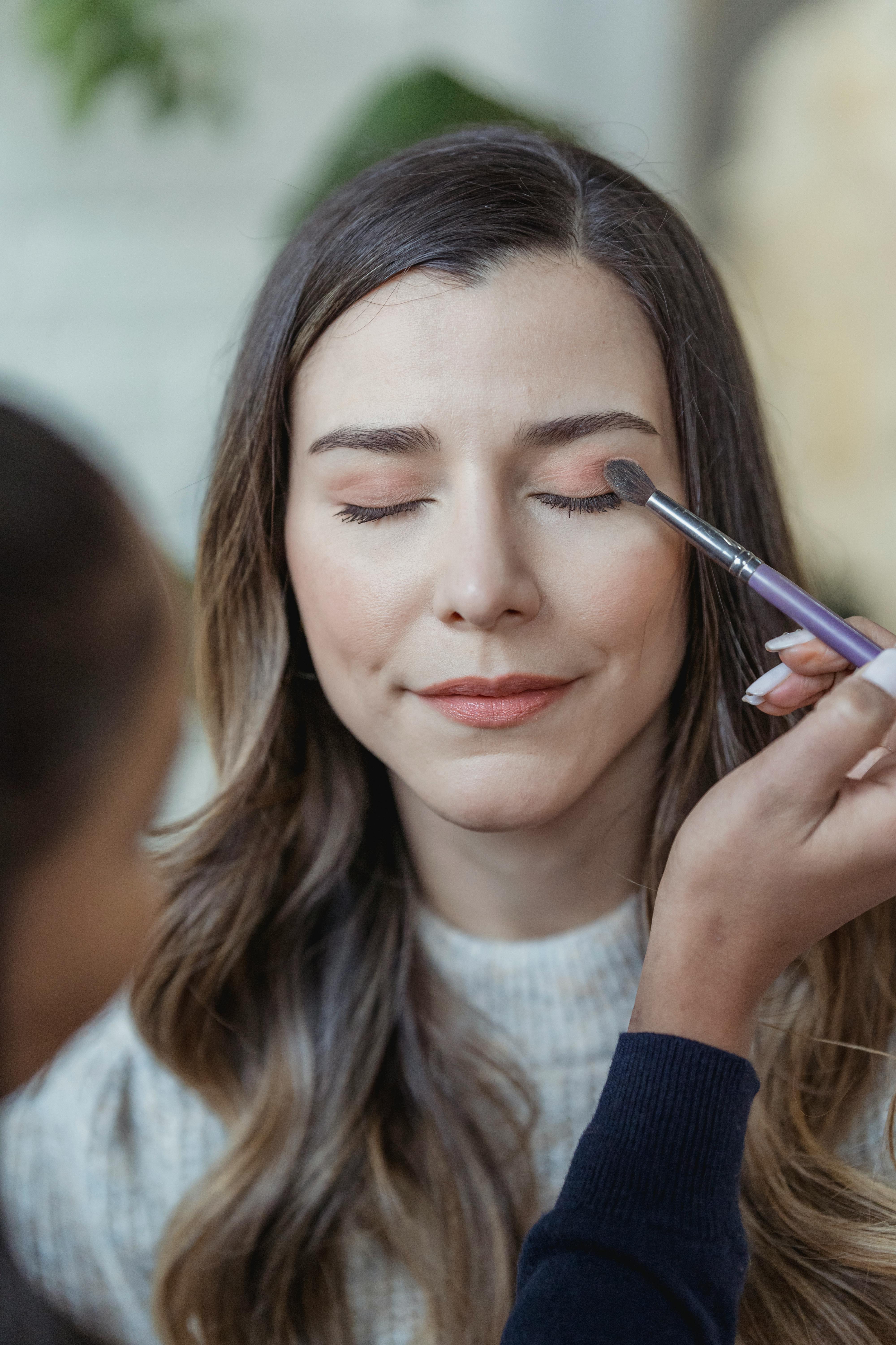 visagiste applying eye makeup on content clients face