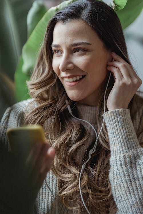 Crop smiling woman listening to music in earphones