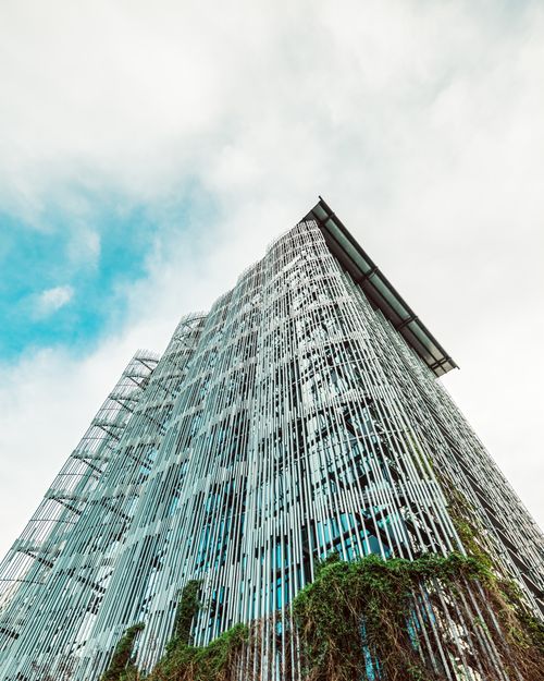 Free From below view of modern futuristic building made of glass and metal covered with unusual green plants under blue cloudy sky at daytime Stock Photo