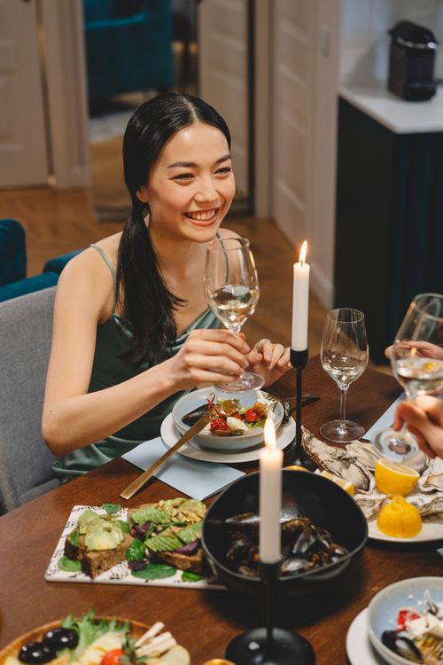 Free Joyful woman enjoying a dinner party with friends, surrounded by candlelight and gourmet food. Stock Photo