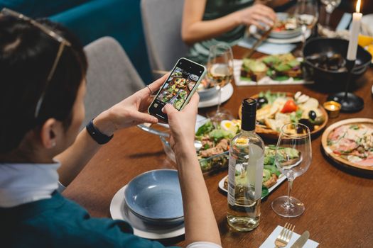 A person taking photos of a delicious dinner with wine, showcasing a vibrant dining scene indoors.